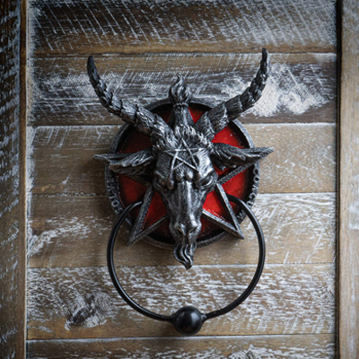 A door knocker in the shape of Baphomet the goat deity inside a surrounding pentagram is placed on a door.