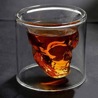 A crystal skull shot glass is displayed with liqueur poured inside of it makes the inner grinning skull glow.