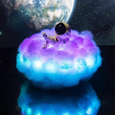 A night lamp in a cloud shape on which an astronaut is lying is displayed. The cloud is ambiently llit with blue and purple colors, it looks so cool.