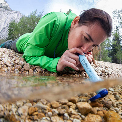 A boy drinking water from a water stream through LifeStraw water filter.