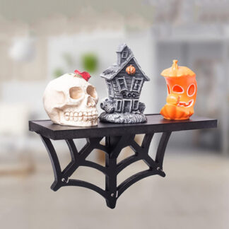 A black floating shelf, the support bottom part of which is in the form of a black spider web, is represented and on the shelf there are three objects which are a skull, a cartoon-like scary house and a half eaten pumpkin lantern with a smiling face on it.