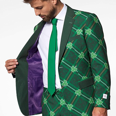 A handsome model is wearing a suit with shamrock patterns all over it. The pants and the jacket have identical patterns while the tie is green. It's a perfect outfit for St. Patrick's Day.