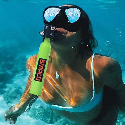 A woman diving underwater is viewed with a portable scuba diving tank attached to her mouth.