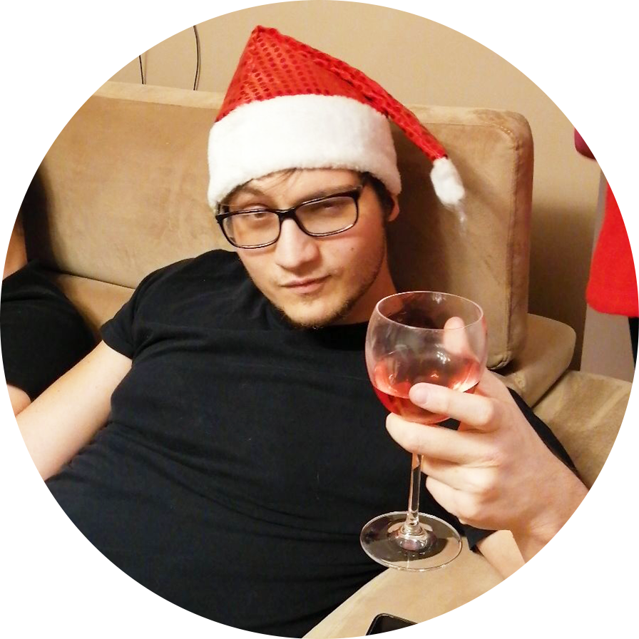 Tyler Redlev who is the founder of santagotgeek.com is sitting on a couch with a red santa hat on his head and holds a glass of red wine on his hand.