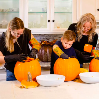 Two women and a child scraping pumpkins in the kitchen with pumpkin scraping gloves.
