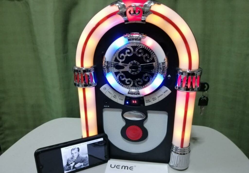 The UEME brand retro tabletop jukebox is displayed on a table with a mobile phone placed next to it for scale.